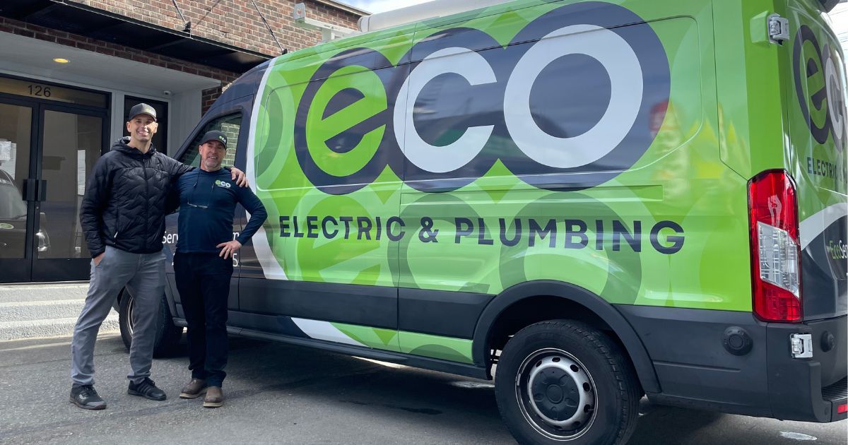 The image shows two employees of eco services standing in front of eco electrical and plumbing company van.